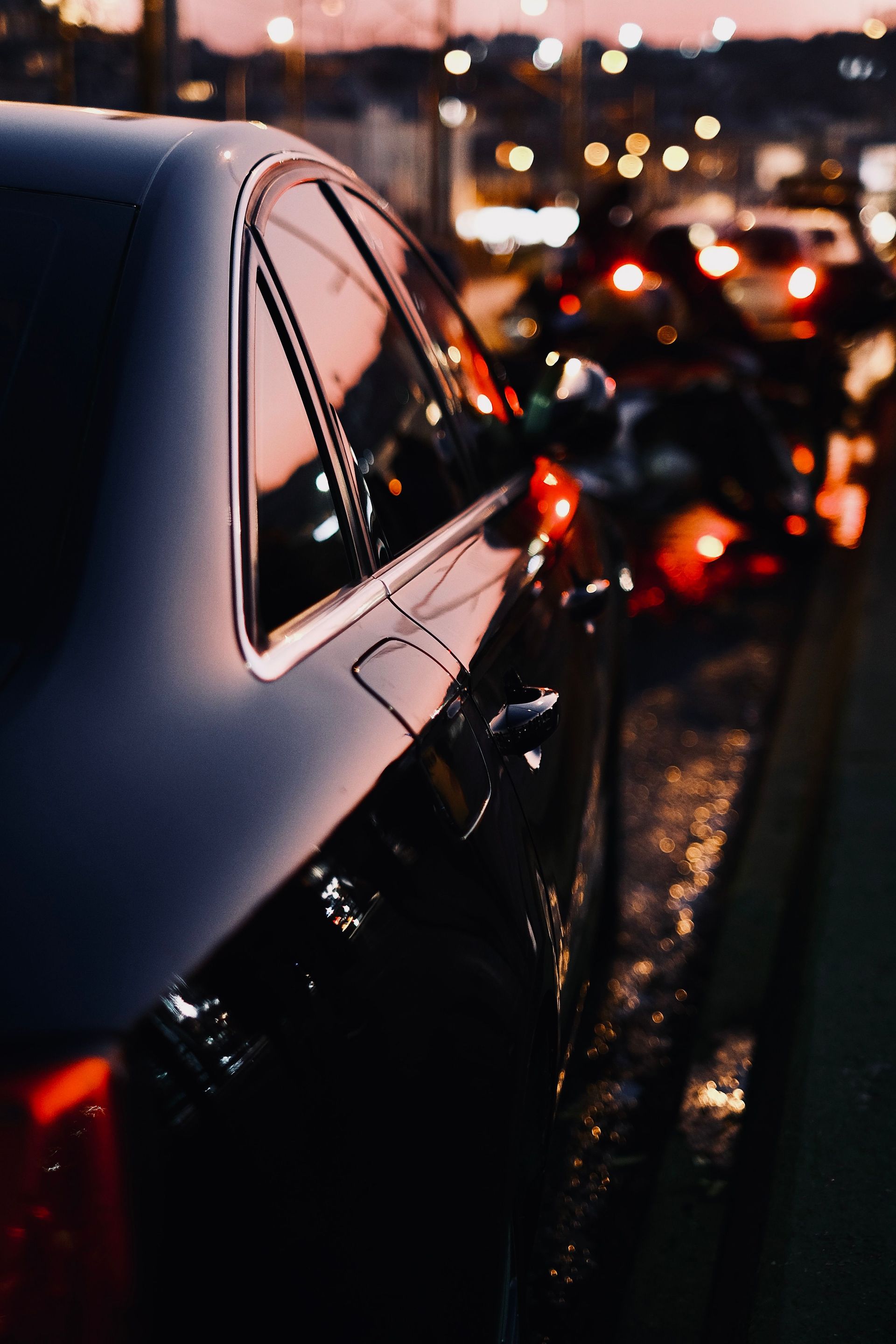 A sleek black luxury car with reflections at twilight in a busy city street.