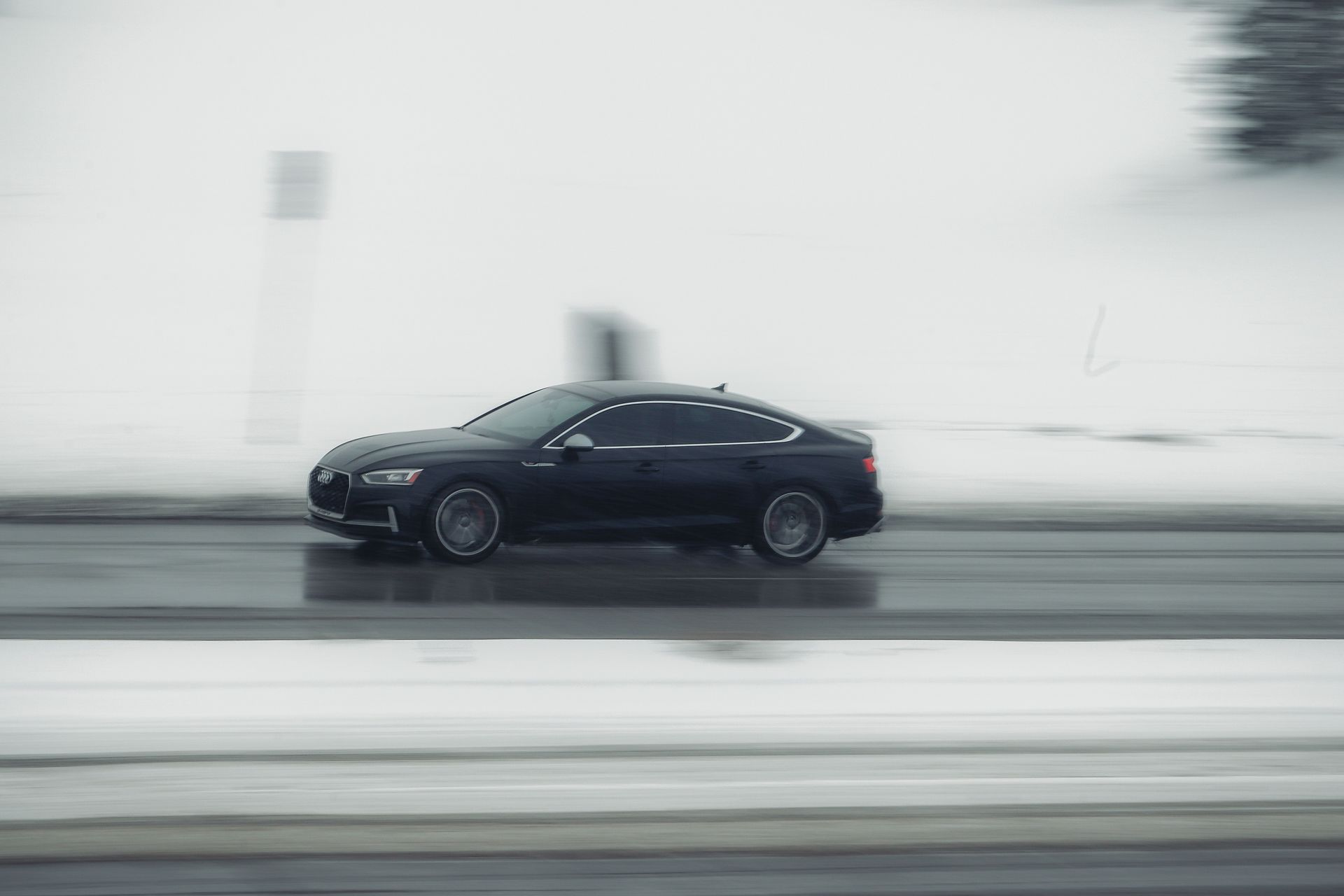 Black luxury car driving at high speed on a snowy road in Calgary, Canada during winter.