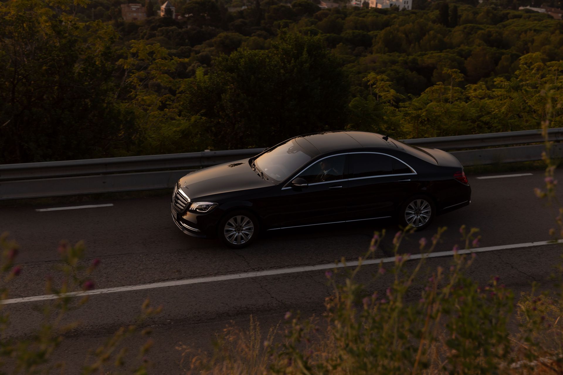 Elegant black luxury sedan driving on a picturesque forest road during daytime.